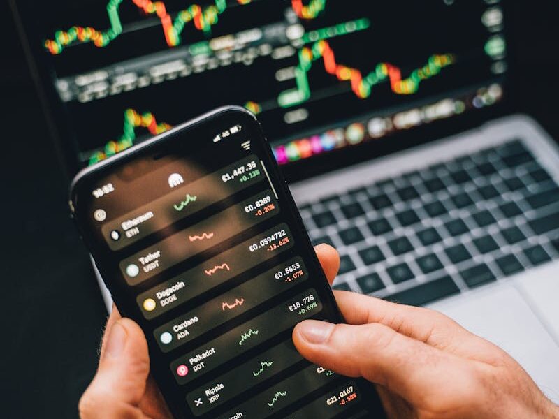 Hands holding smartphone with stock app, laptop displaying charts. Perfect for financial and technology themes.